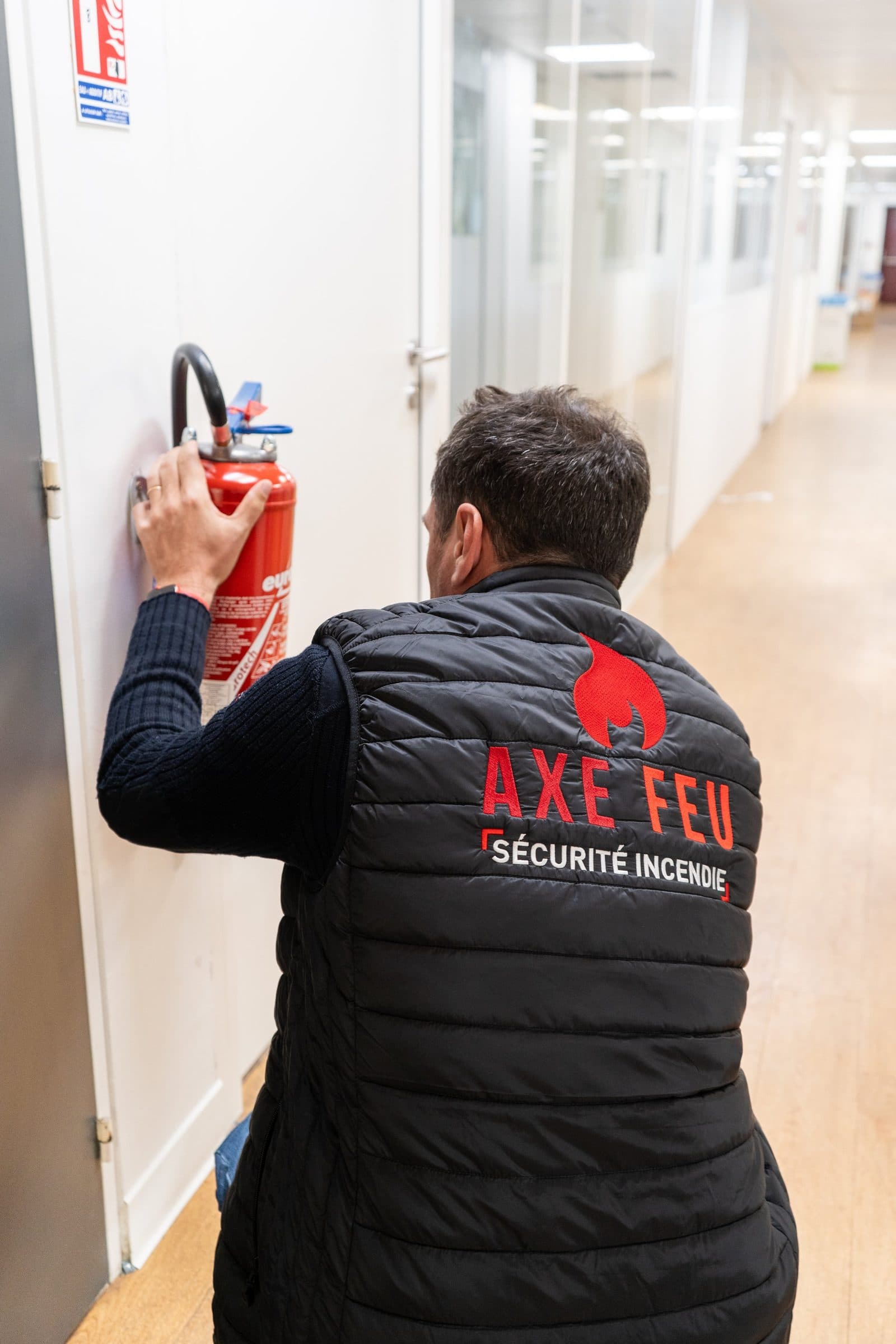 Technicien AXE FEU contrôlant un extincteur mural lors d'une visite de prévention incendie dans les Yvelines